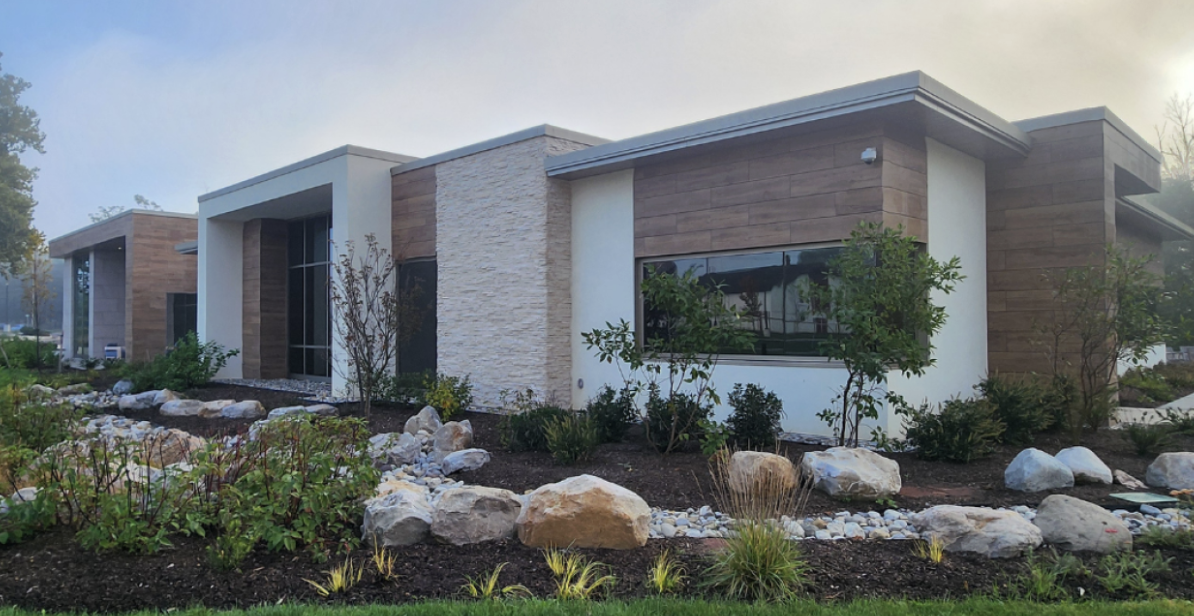 Modern healthcare facility building surrounded by landscaped gardens and walking paths.